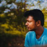 Thoughtful young man in a blue shirt outdoors in TN, India, surrounded by vibrant nature.