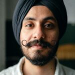 Close-up portrait of a confident young man wearing a turban and mustache, exuding style and individuality.